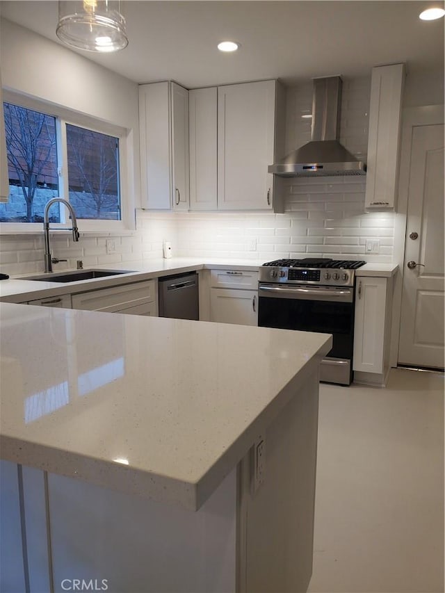 kitchen featuring a sink, white cabinets, appliances with stainless steel finishes, wall chimney range hood, and backsplash