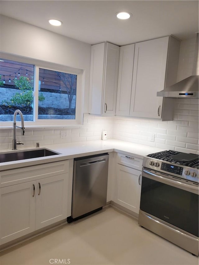 kitchen with backsplash, white cabinets, stainless steel appliances, wall chimney exhaust hood, and a sink