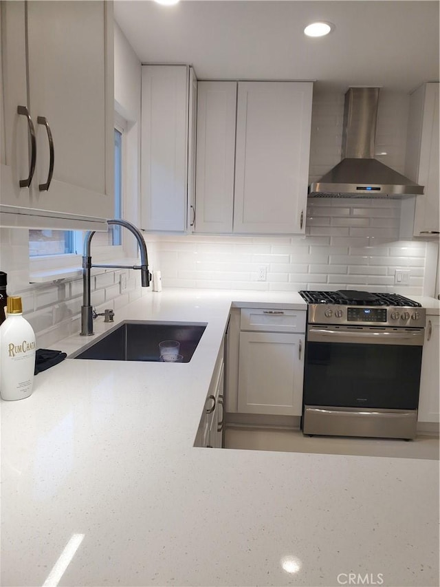 kitchen featuring backsplash, stainless steel range with gas cooktop, wall chimney range hood, white cabinetry, and a sink