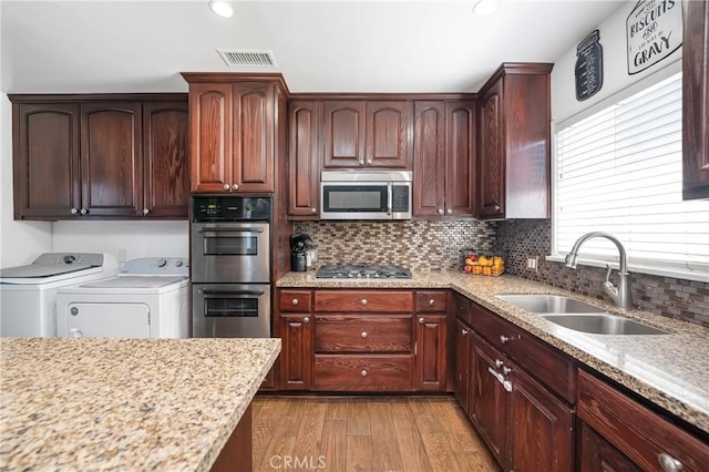 kitchen featuring a sink, visible vents, appliances with stainless steel finishes, independent washer and dryer, and light wood finished floors