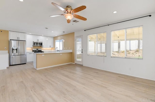 kitchen featuring appliances with stainless steel finishes, hanging light fixtures, light hardwood / wood-style floors, white cabinetry, and kitchen peninsula