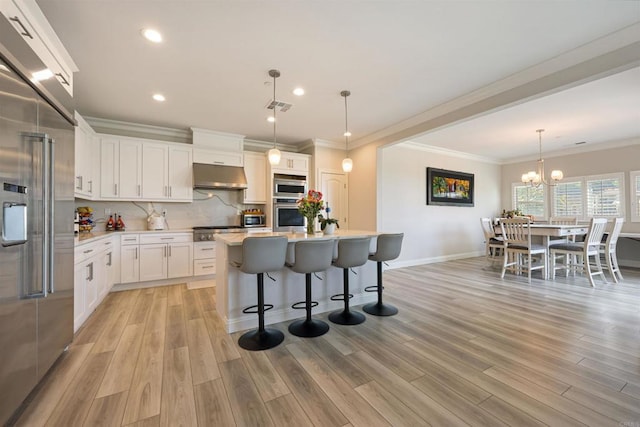 kitchen with built in appliances, a center island, white cabinetry, pendant lighting, and a kitchen breakfast bar