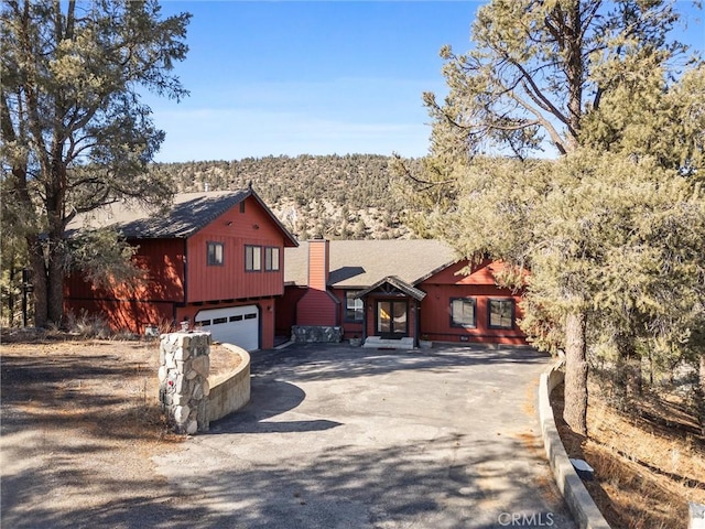 rustic home with a garage, driveway, and a chimney