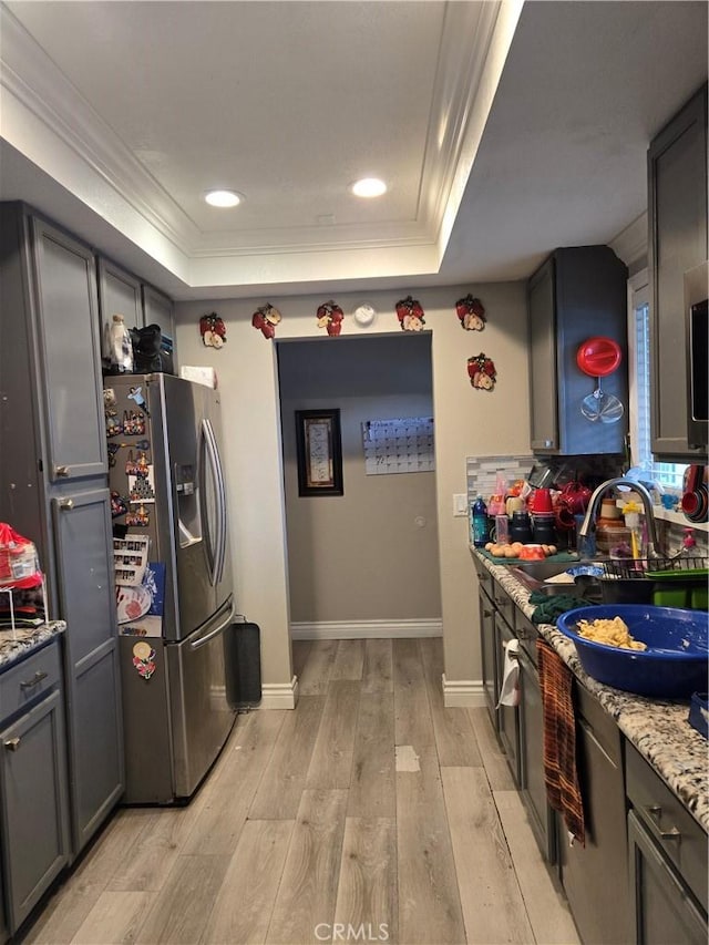 kitchen featuring stainless steel fridge with ice dispenser, light hardwood / wood-style flooring, light stone counters, a raised ceiling, and crown molding