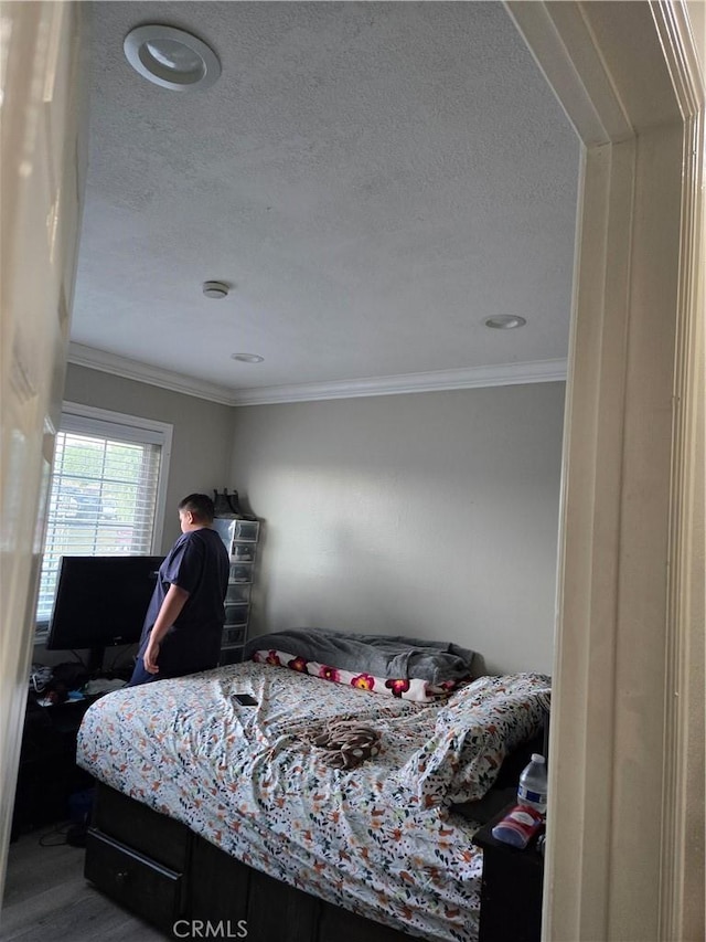 bedroom with a textured ceiling, ornamental molding, and wood-type flooring