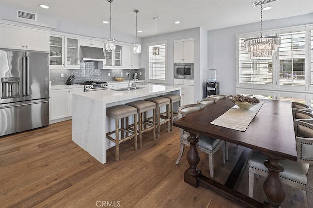 kitchen featuring stainless steel appliances, white cabinets, pendant lighting, sink, and a kitchen island with sink