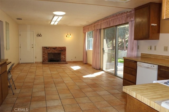 kitchen with light tile patterned floors, brown cabinetry, dishwasher, light countertops, and a fireplace