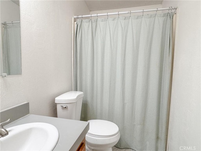 bathroom featuring a textured wall, vanity, and toilet