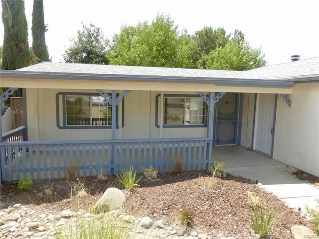 view of exterior entry with fence, an attached carport, and roof with shingles