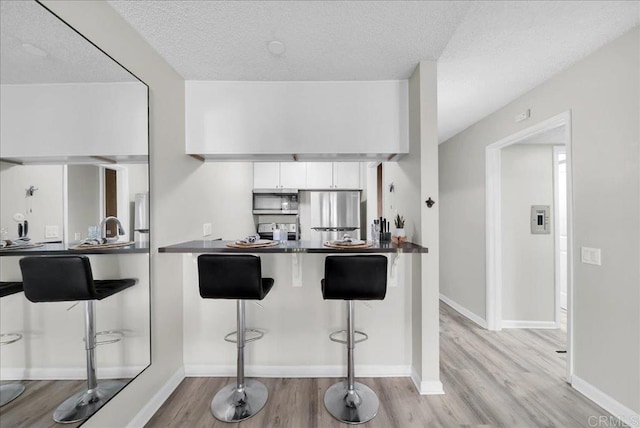 kitchen with light wood-type flooring, kitchen peninsula, stainless steel appliances, a breakfast bar, and white cabinets