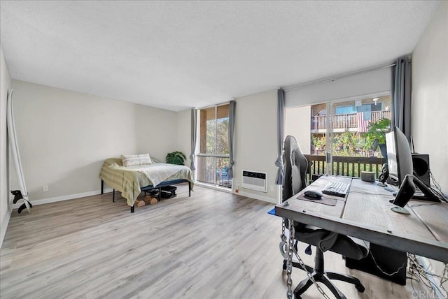 bedroom with light hardwood / wood-style flooring, a wall unit AC, multiple windows, and access to exterior