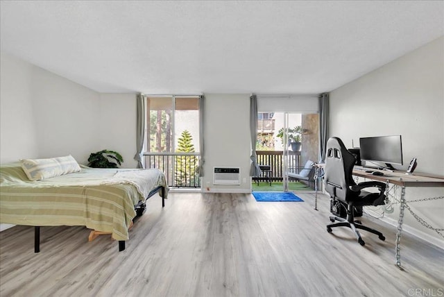 bedroom with heating unit, access to outside, and light hardwood / wood-style floors