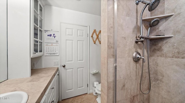 bathroom with toilet, a tile shower, vanity, and tile patterned floors