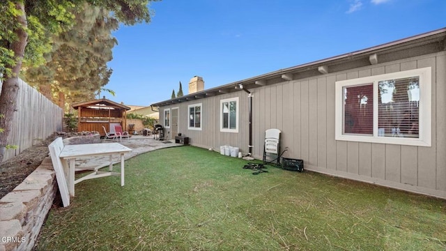 rear view of property featuring a hot tub, a fenced backyard, a chimney, a yard, and a patio area