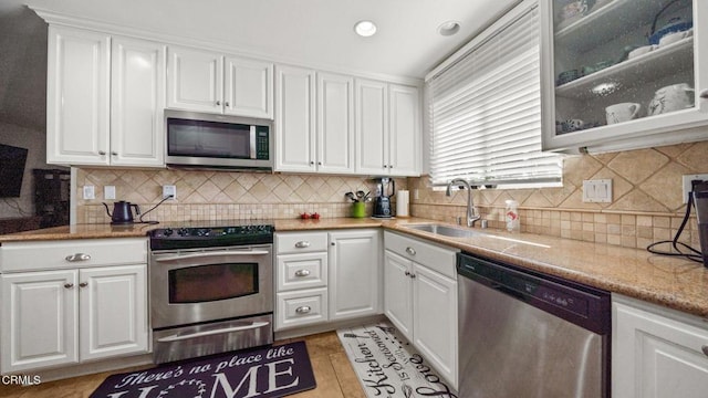 kitchen with light tile patterned floors, white cabinets, glass insert cabinets, appliances with stainless steel finishes, and a sink