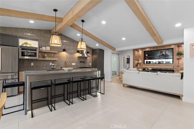 kitchen featuring vaulted ceiling with beams, a breakfast bar area, built in fridge, hanging light fixtures, and dark countertops