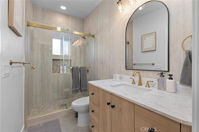 bathroom with toilet, a stall shower, tile walls, and vanity