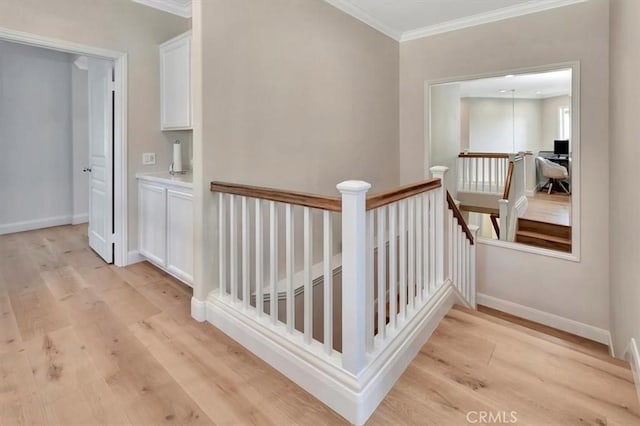 hall with baseboards, light wood finished floors, an upstairs landing, and crown molding