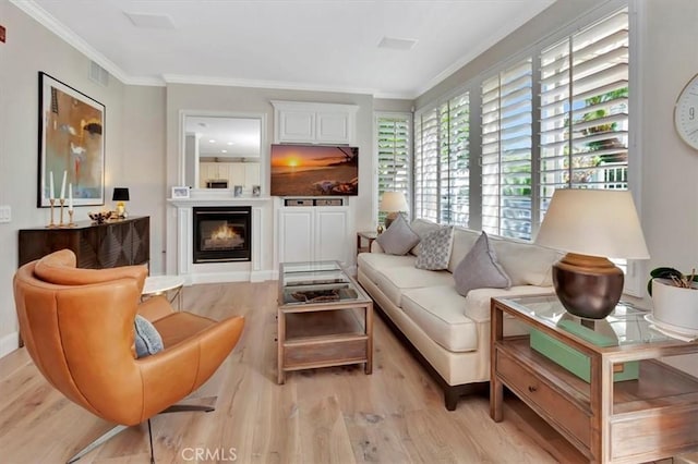 interior space with light wood-style floors, visible vents, ornamental molding, and a glass covered fireplace