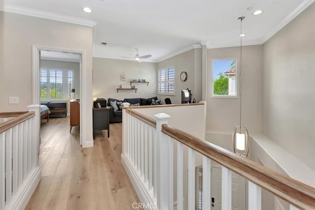 hall with crown molding, light wood-type flooring, an upstairs landing, and a healthy amount of sunlight