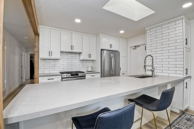 kitchen with white cabinetry, stainless steel appliances, sink, backsplash, and a kitchen breakfast bar