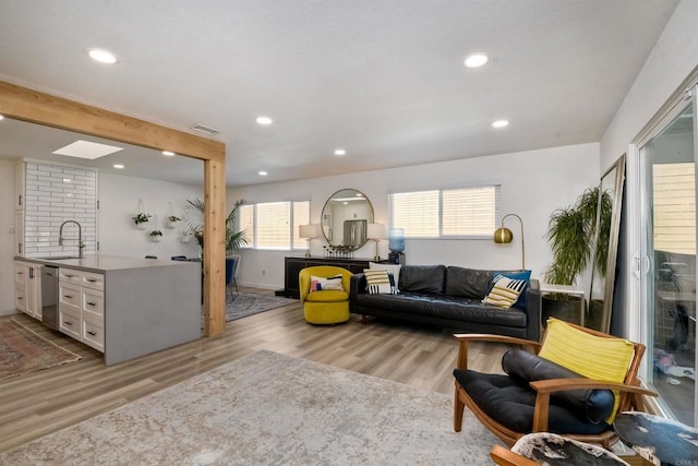 living room featuring sink, a skylight, beamed ceiling, and light hardwood / wood-style floors