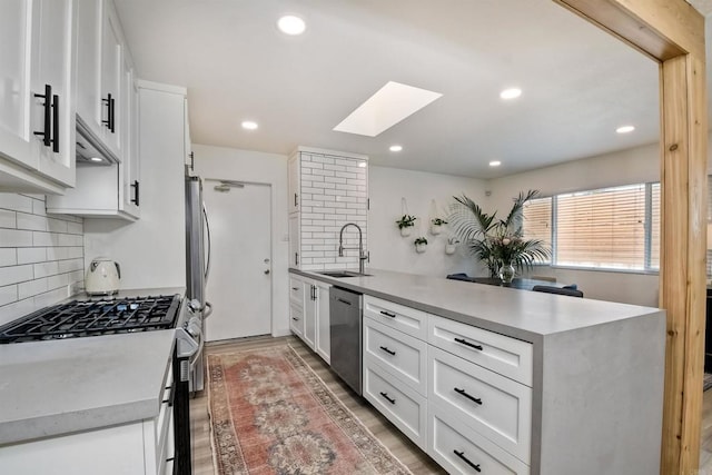 kitchen with sink, a skylight, wall chimney range hood, stainless steel appliances, and white cabinets