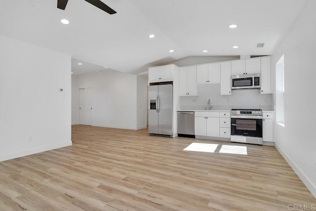 kitchen with light wood-type flooring, stainless steel appliances, sink, vaulted ceiling, and white cabinets