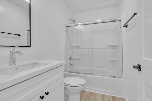 full bathroom with hardwood / wood-style floors, bath / shower combo with glass door, vanity, and toilet