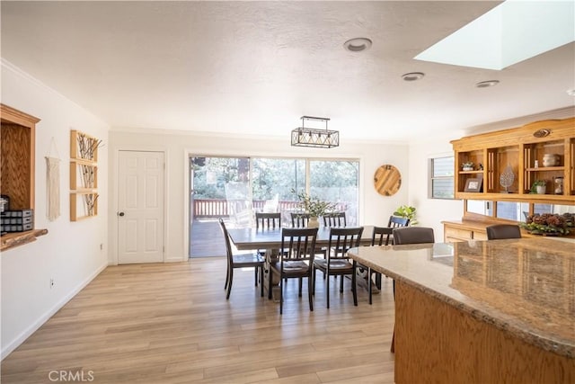 dining area with light hardwood / wood-style flooring, a skylight, and ornamental molding