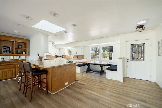 kitchen featuring white cabinetry, light stone countertops, light hardwood / wood-style floors, ornamental molding, and a skylight