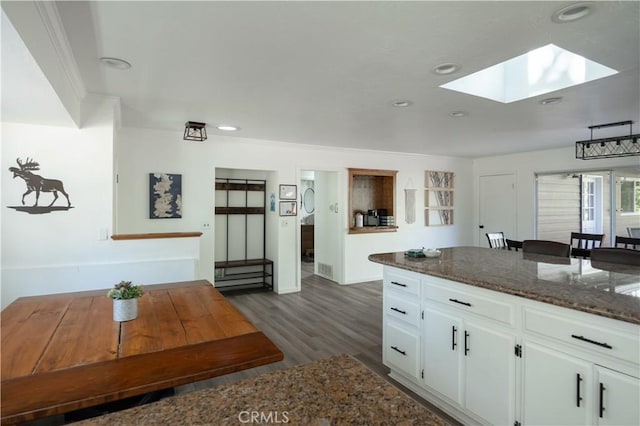 kitchen with dark stone countertops, white cabinets, a skylight, and dark hardwood / wood-style flooring