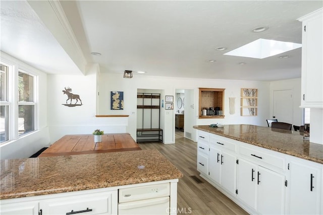 kitchen featuring white cabinets, a skylight, dark stone countertops, and light hardwood / wood-style flooring