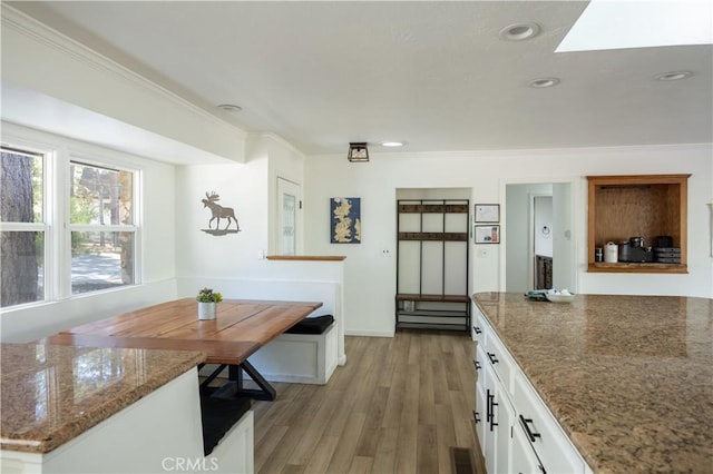 kitchen featuring white cabinets, light hardwood / wood-style flooring, crown molding, and stone counters