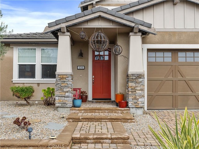 property entrance with stucco siding, a tile roof, stone siding, board and batten siding, and an attached garage