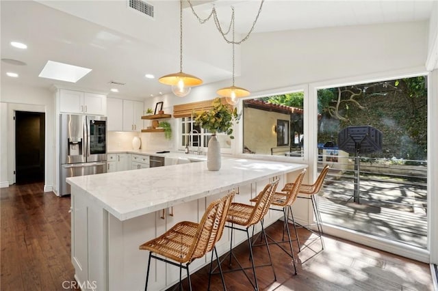 kitchen featuring a skylight, stainless steel refrigerator with ice dispenser, open shelves, hanging light fixtures, and white cabinets