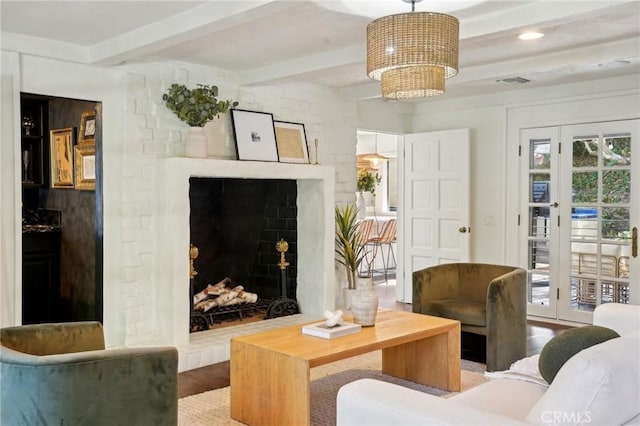 living area with visible vents, wood finished floors, an inviting chandelier, a fireplace, and beam ceiling