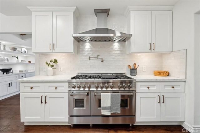 kitchen featuring wall chimney exhaust hood, light stone countertops, white cabinets, and double oven range