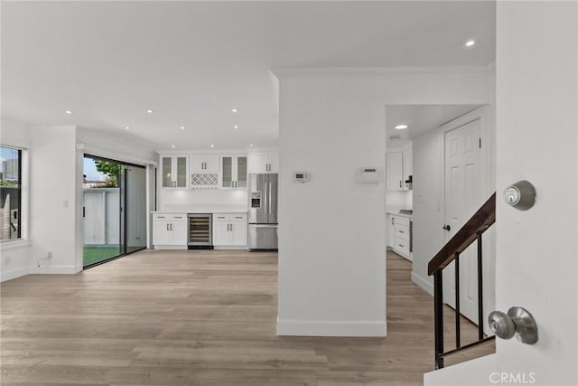 kitchen with stainless steel refrigerator with ice dispenser, light hardwood / wood-style floors, ornamental molding, white cabinets, and beverage cooler