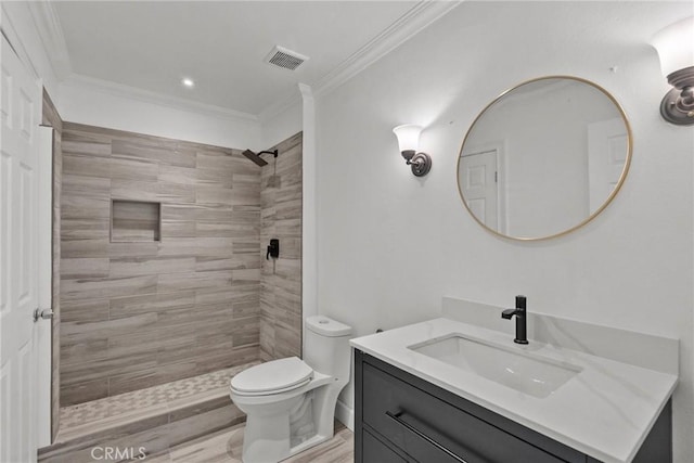 bathroom featuring wood-type flooring, toilet, tiled shower, crown molding, and vanity