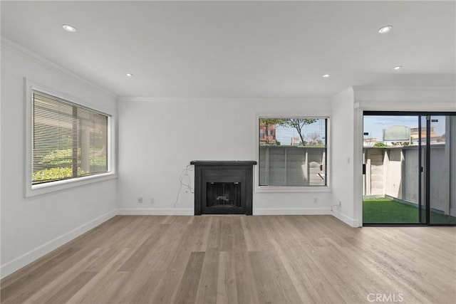 unfurnished living room with light wood-type flooring, crown molding, and a wealth of natural light