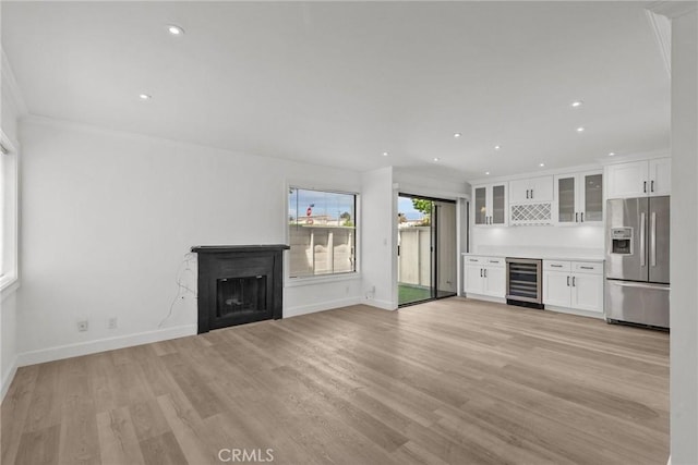 unfurnished living room with ornamental molding, light hardwood / wood-style flooring, wine cooler, and bar