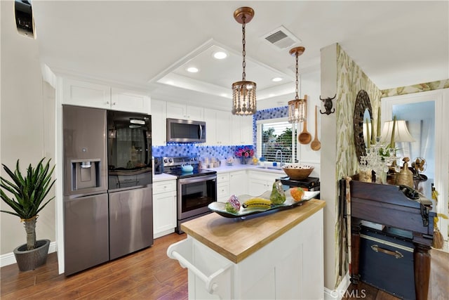 kitchen with appliances with stainless steel finishes, white cabinetry, pendant lighting, and butcher block countertops