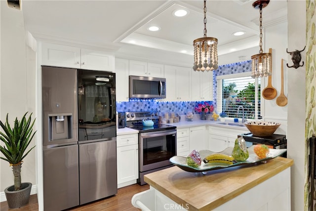 kitchen with a tray ceiling, decorative light fixtures, butcher block counters, appliances with stainless steel finishes, and white cabinetry