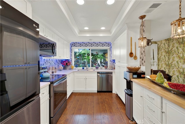 kitchen with appliances with stainless steel finishes, butcher block counters, white cabinets, pendant lighting, and a tray ceiling