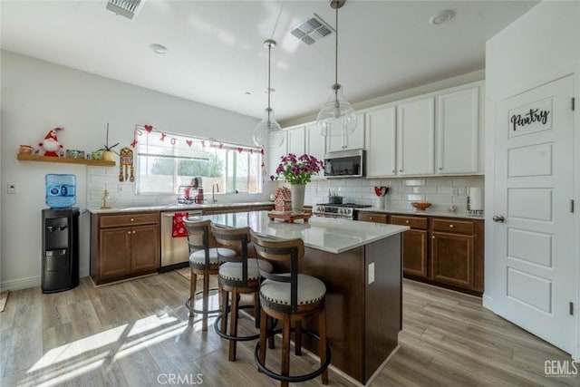 kitchen with white cabinetry, stainless steel appliances, a center island, decorative light fixtures, and a breakfast bar area