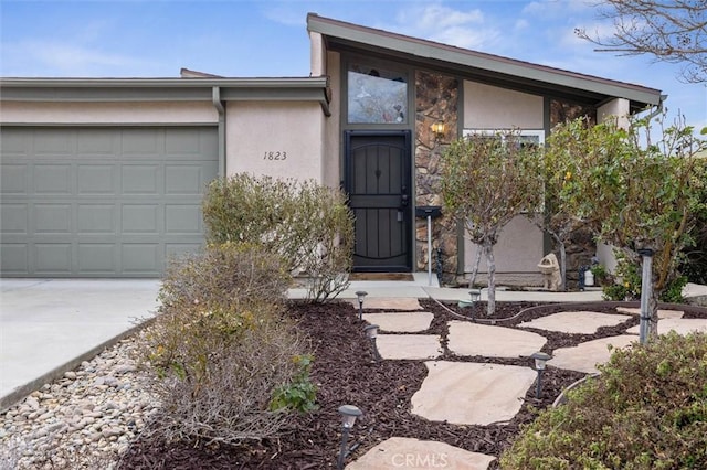 view of exterior entry with a garage, concrete driveway, and stucco siding