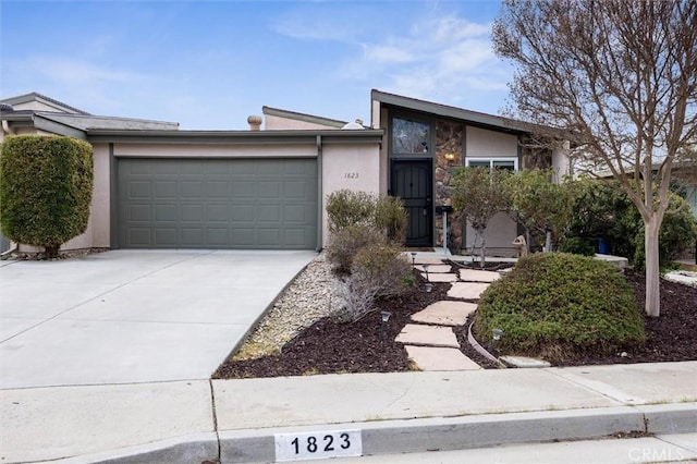 view of front of home featuring an attached garage, stone siding, concrete driveway, and stucco siding