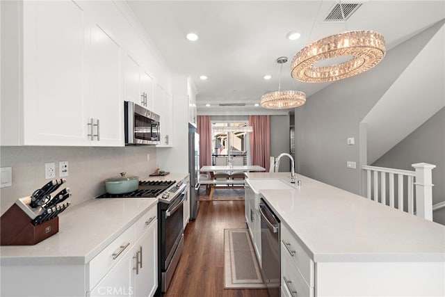 kitchen with stainless steel appliances, an island with sink, white cabinets, decorative light fixtures, and dark hardwood / wood-style flooring