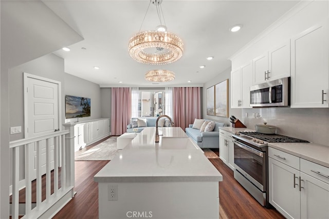 kitchen featuring a center island with sink, stainless steel appliances, a chandelier, pendant lighting, and white cabinetry